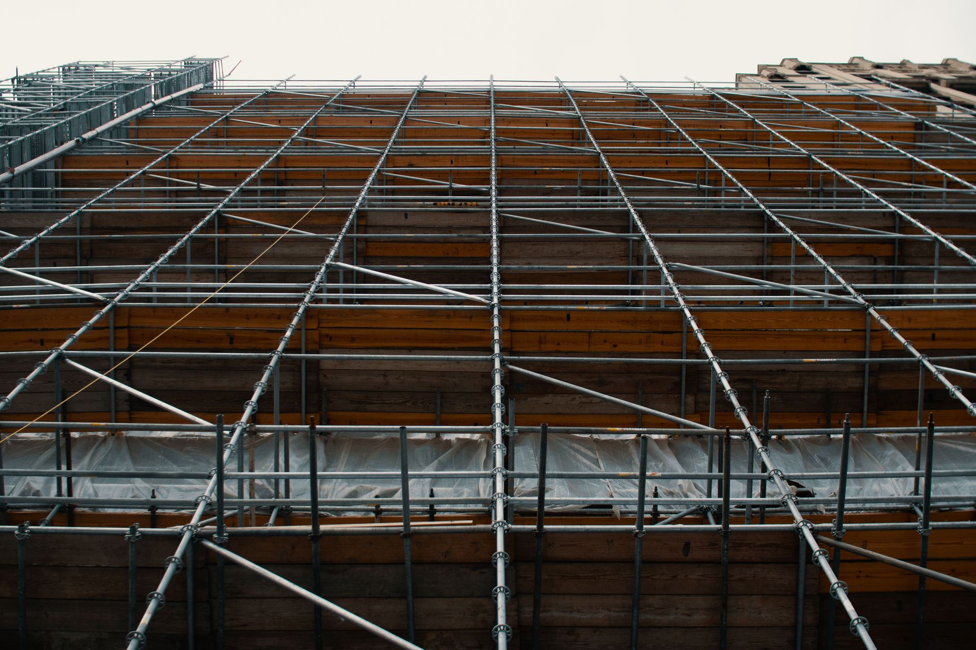 Low angle view of metal scaffolding standing near repairing building against cloudy sky